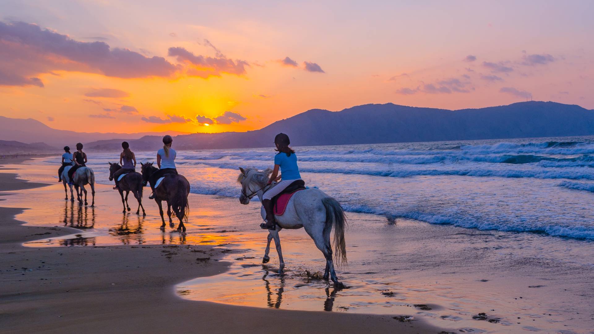 group horseback riding on the beach at sunset